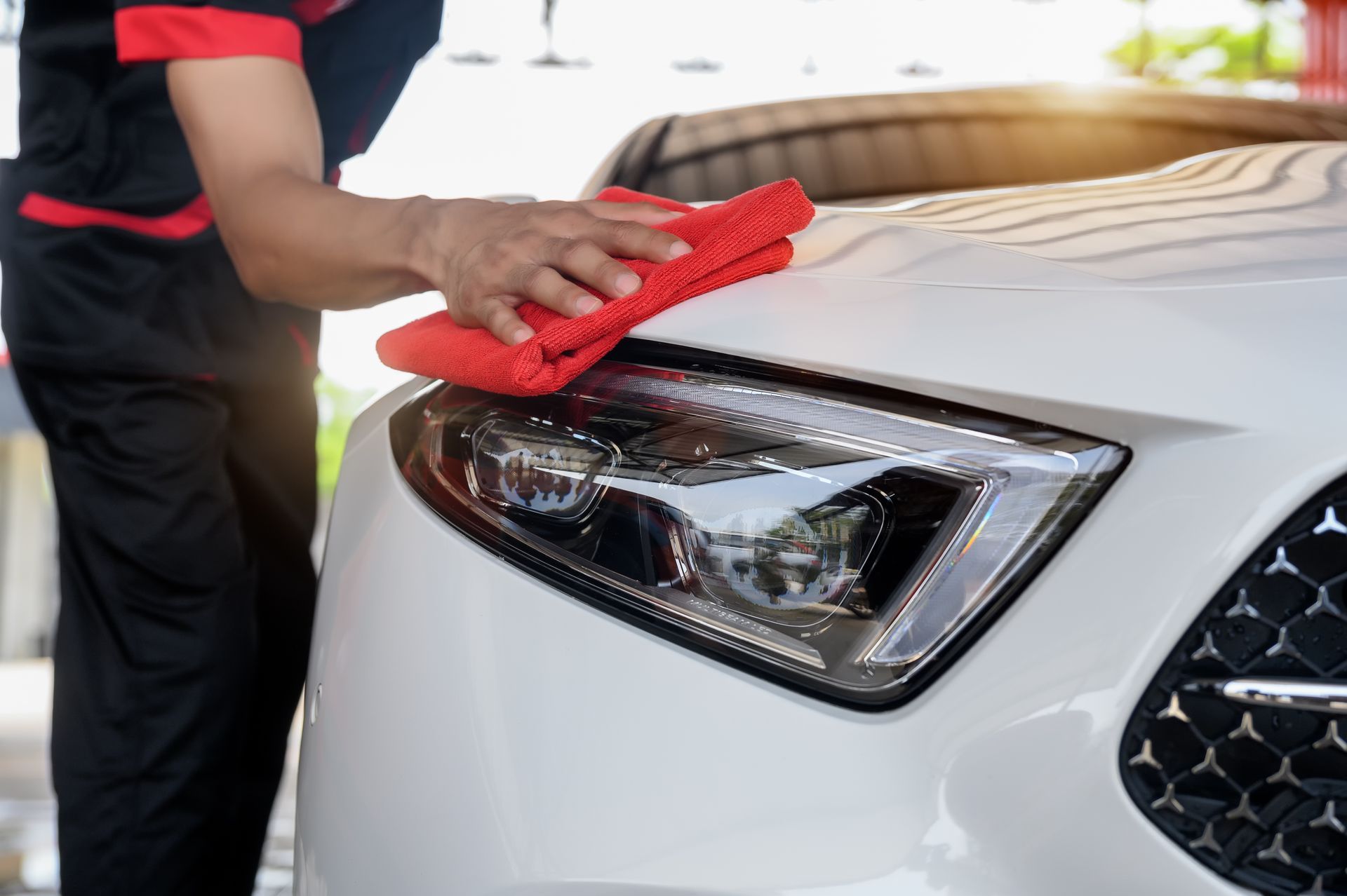 Person wiping a white car’s headlight and hood with a red cloth