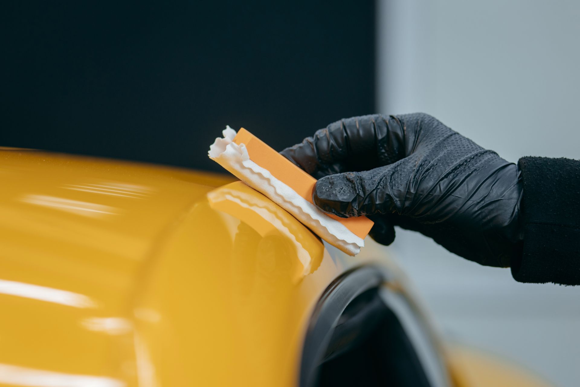 Gloved hand using a sanding block on a yellow car surface, likely during auto body repair