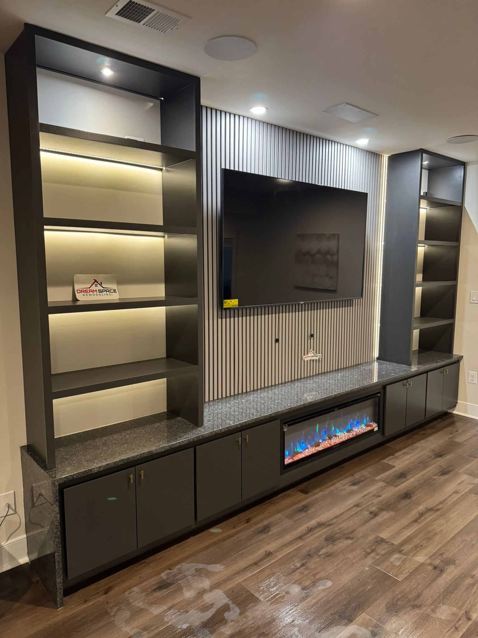 Modern basement media wall in Reisterstown, MD with LED-lit shelves, electric fireplace, and quartz waterfall countertop