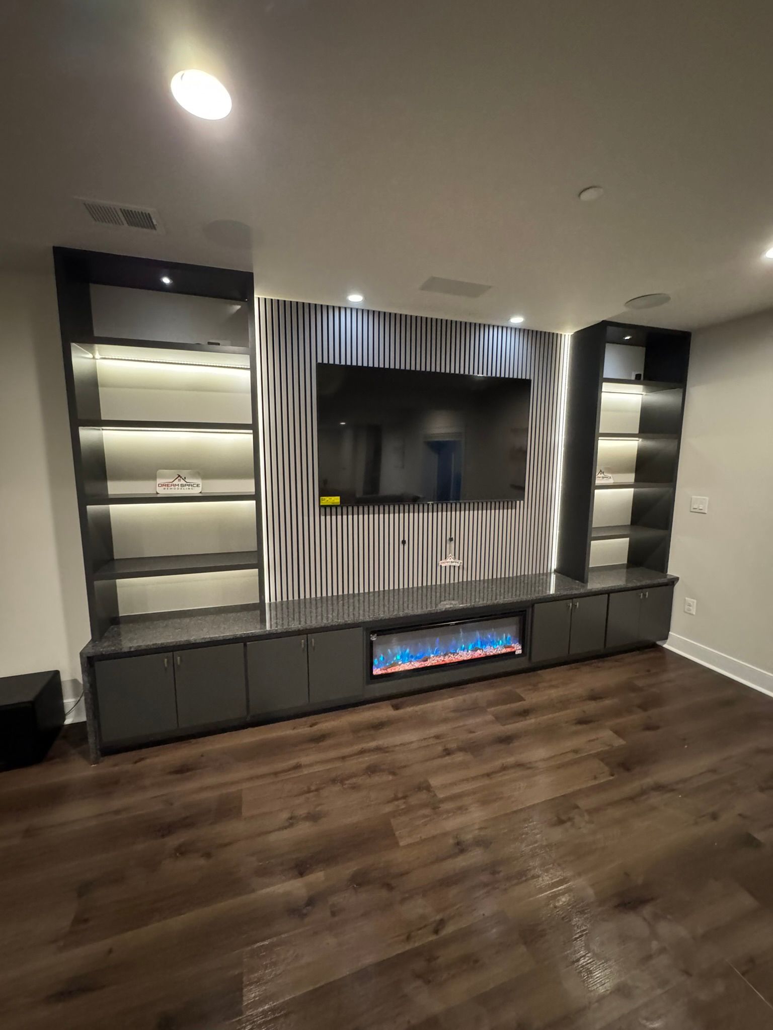 Custom media wall in Reisterstown, MD basement featuring built-in lighting, fireplace, and quartz waterfall design