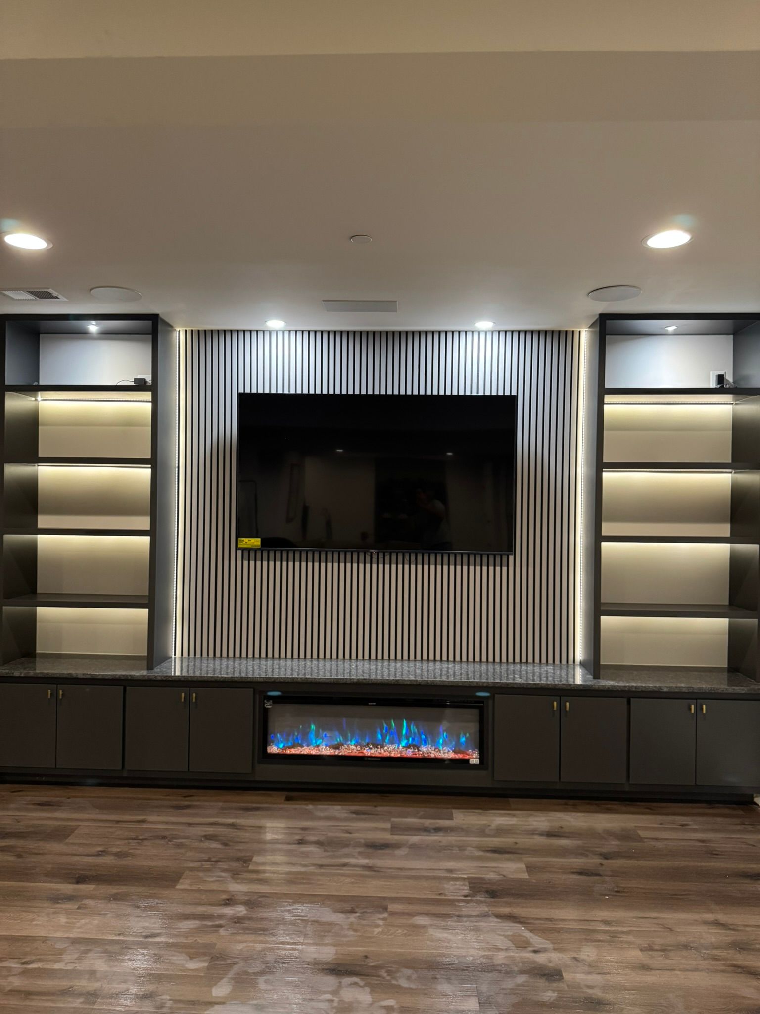 Sleek basement media wall with illuminated shelves, electric fireplace, and quartz waterfall counter in Reisterstown, MD
