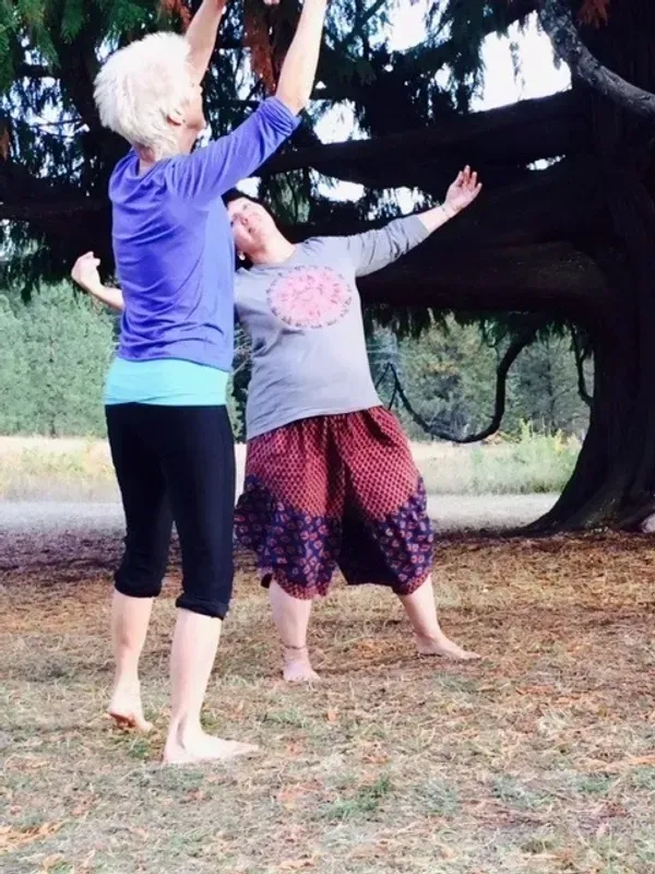 Two people outdoors, reaching up toward tree branches in a grassy area