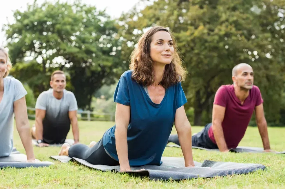 People doing yoga stretches on mats in a grassy park outdoors