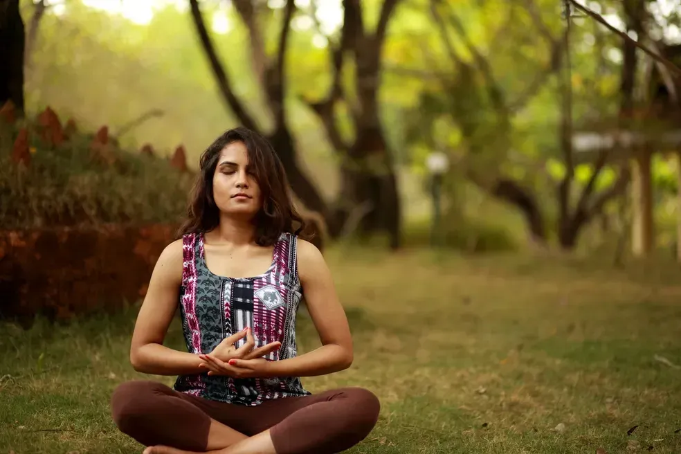 Person sitting cross-legged outdoors on grass, meditating in a green park.