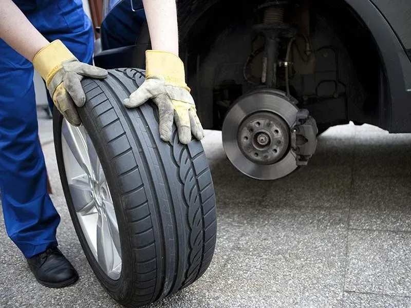 Gloved mechanic fitting a car tire onto a wheel hub with the brake disc visible