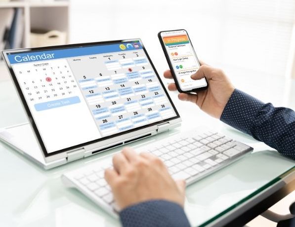 Hands at laptop and computer with calendar on screens
