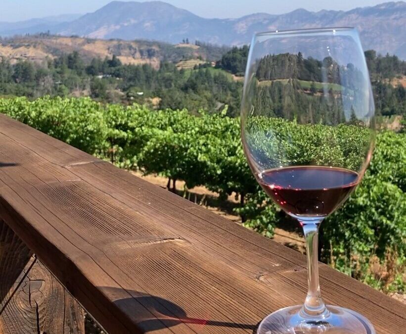 A glass of wine sits on a wooden deck overlooking a vineyard