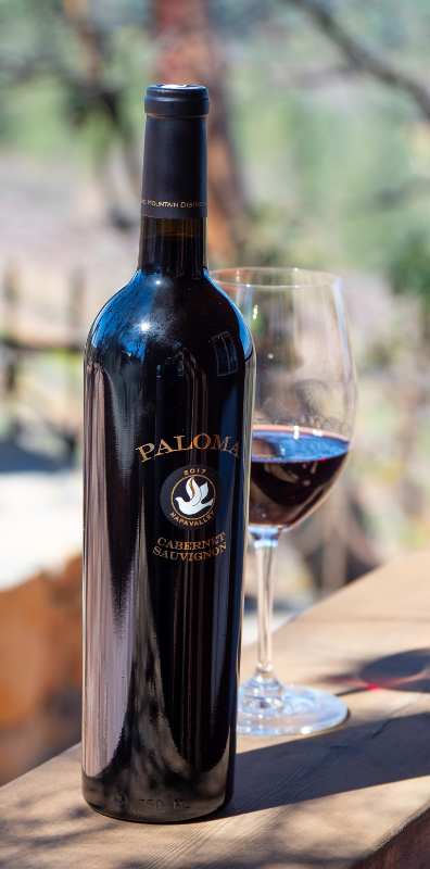A bottle of wine and a glass of wine are sitting on a wooden table.