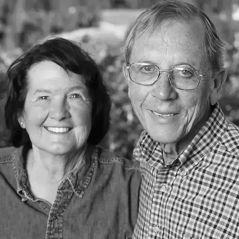 A smiling couple in a close-up black and white portrait, wearing casual shirts outdoors.