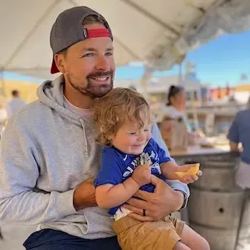 Jace Richards of Paloma Vineyard holding his young son at a winery event, continuing the family legacy in Napa Valley.