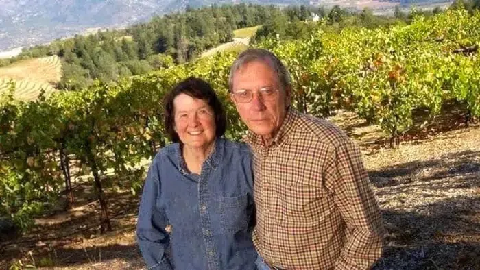 The founders of Paloma Vineyard standing together in a vineyard with rows of grapevines and mountains in the background.