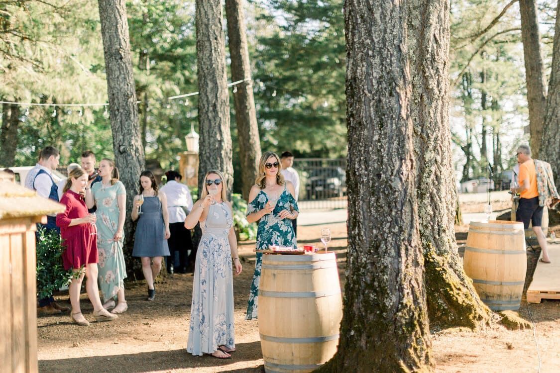 A group of people are standing around wooden barrels in the woods.