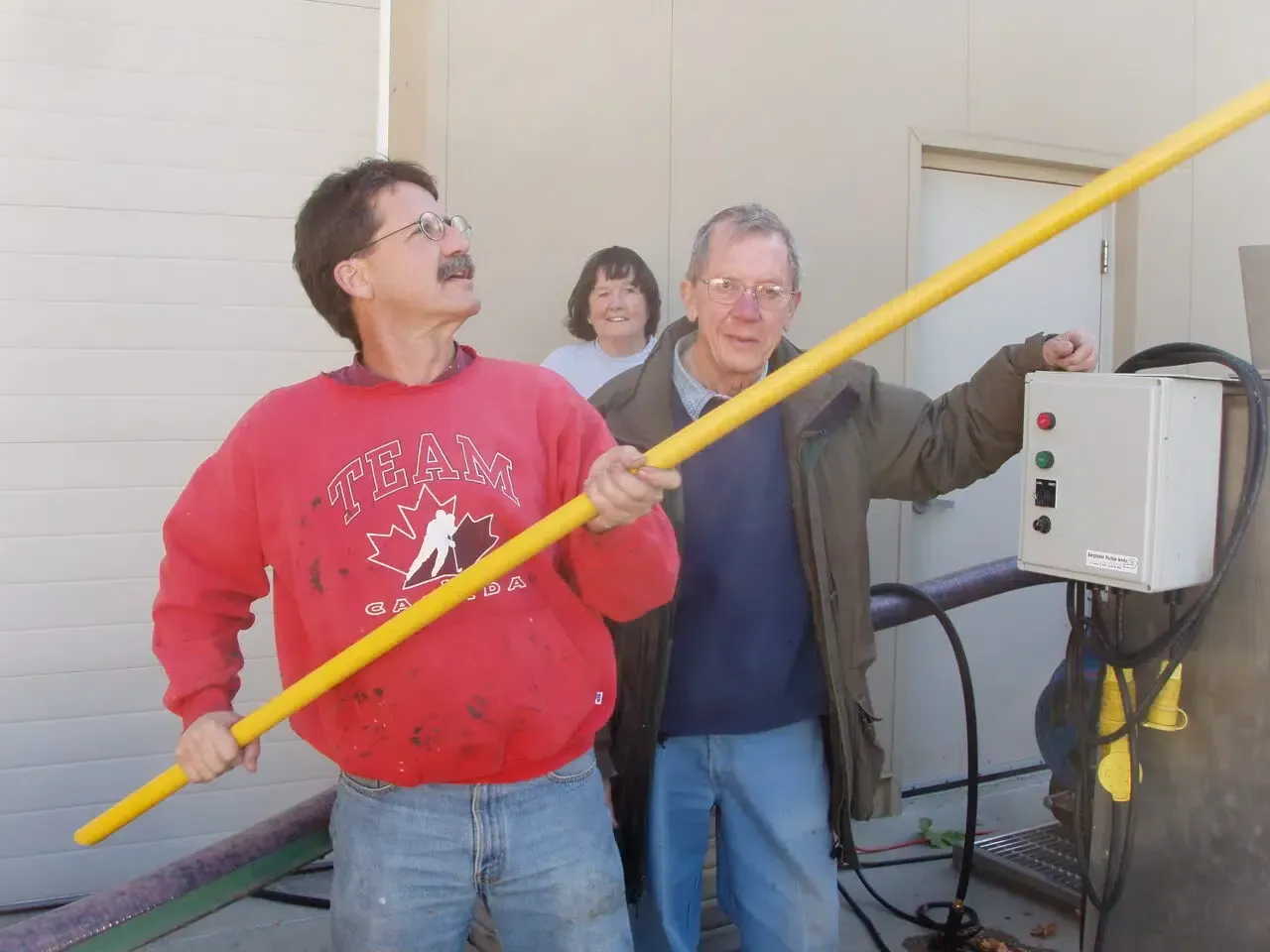 Two men and a woman smiling outdoors at a Napa, California winery, with one man playfully holding a long yellow pole.
