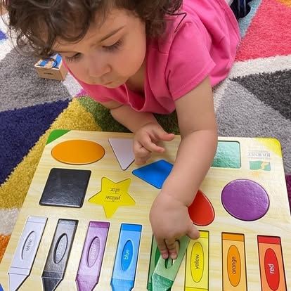 A little girl is playing with a wooden puzzle with crayons on it