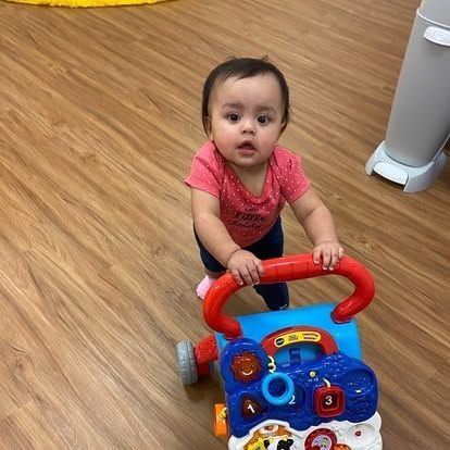A baby is pushing a walker on a wooden floor.