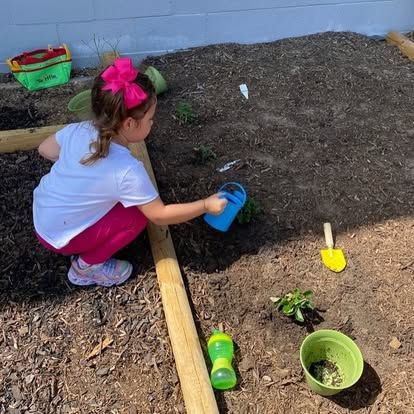 A little girl is kneeling down in the dirt holding a watering can.