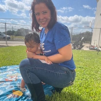A woman is kneeling down in the grass holding a baby.