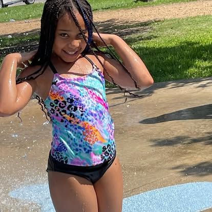 Girl in a vibrant swimsuit, playing in the water on a hot day.
