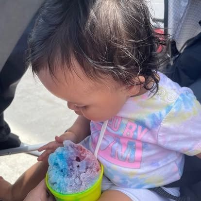 A baby is drinking a cup of ice cream through a straw.