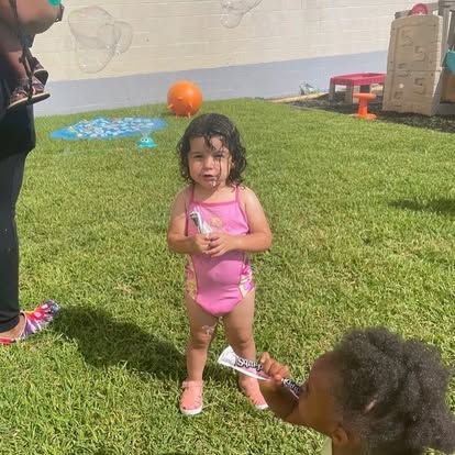 A little girl in a pink bathing suit is standing in the grass.