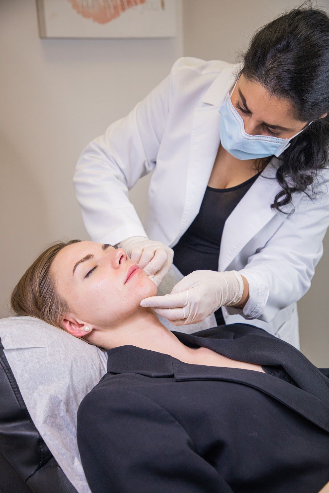 Woman receiving a facial cosmetic procedure from a doctor. Doctor wearing mask, white coat, gloves.