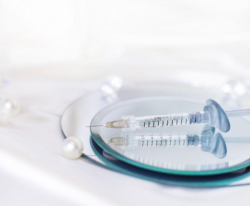 A syringe is sitting on top of a mirror on a wooden floor.