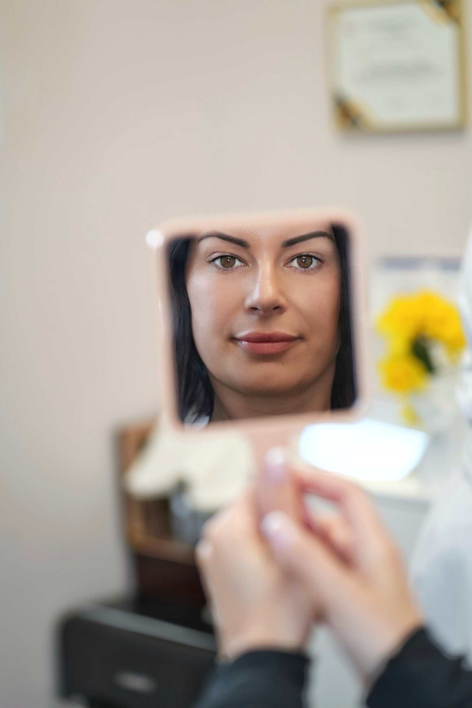 A woman is looking at her face in a mirror.