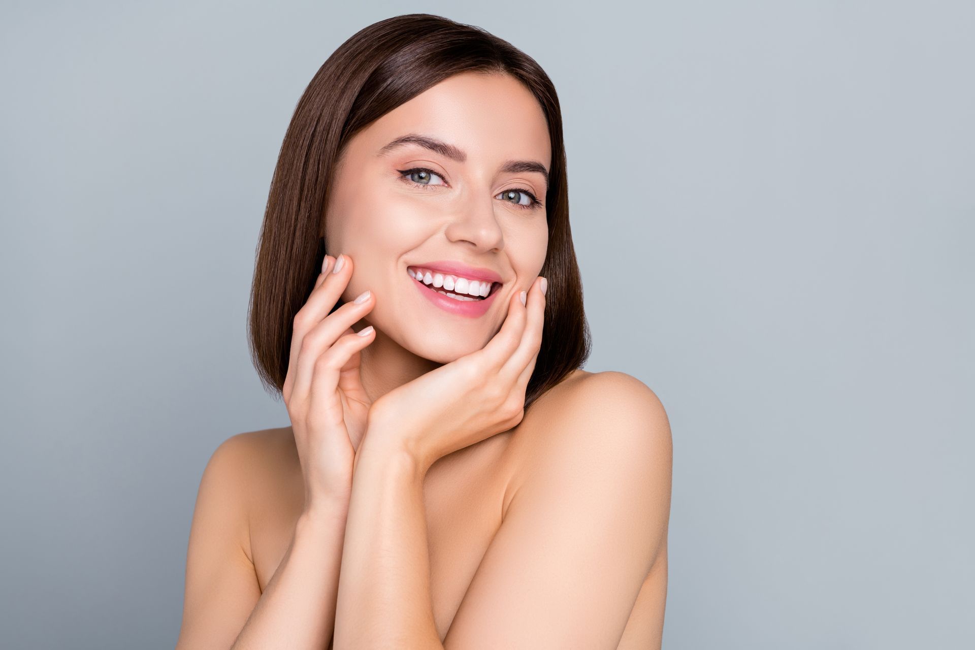 A woman is smiling and touching her face with her hands.