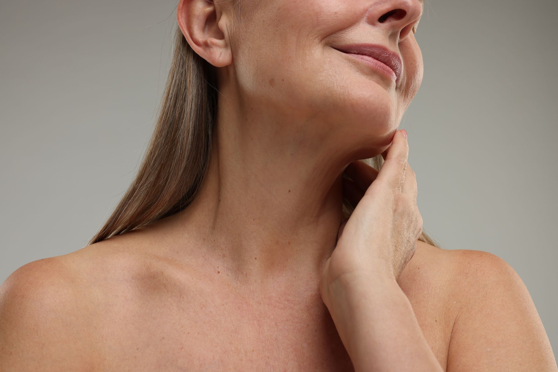 A woman is touching her neck with her hands and smiling.