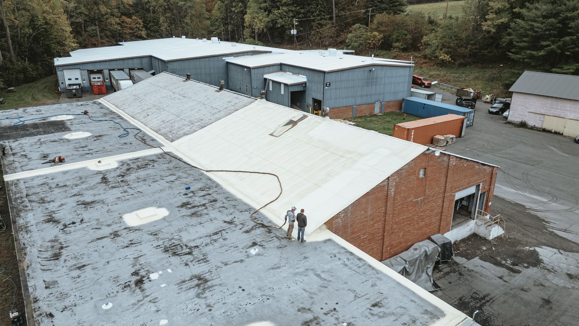 Overhead view of several industrial buildings with people on a rooftop inspecting the structure.