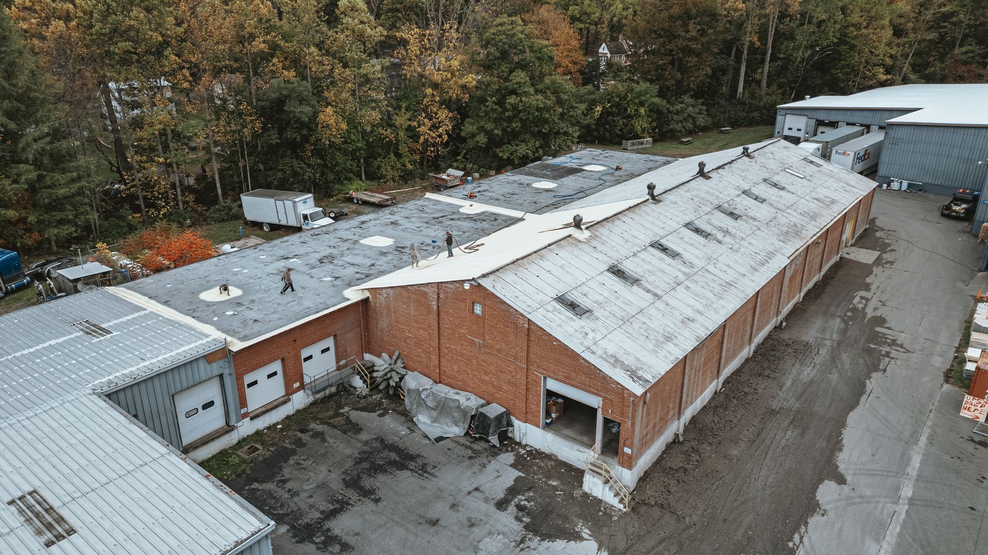 Aerial view of a long brick and metal industrial building with several loading bays, surrounded by trees.