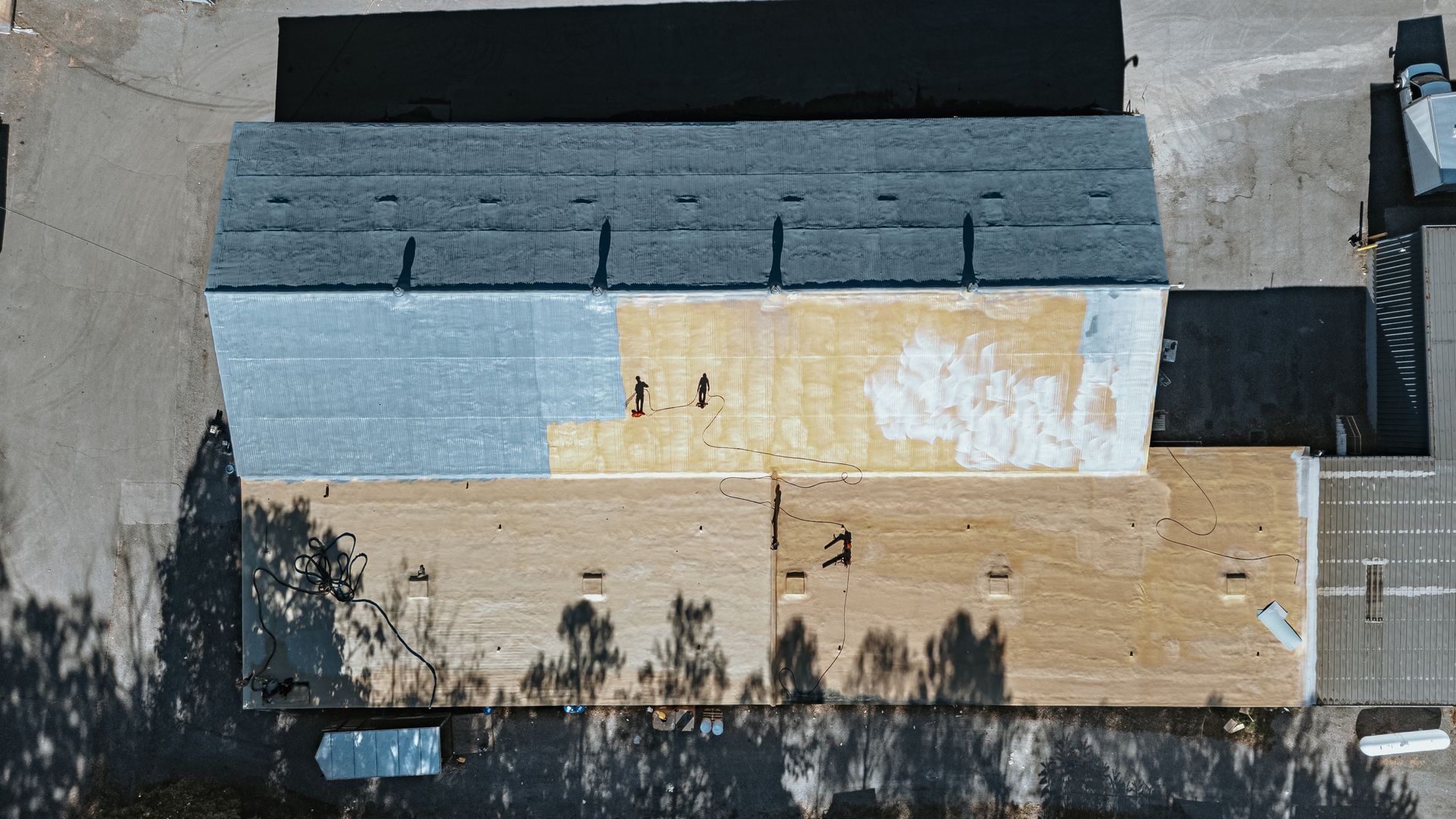 Overhead view of a building with a multi-tone roof. Concrete ground with shadows, a truck, and barriers.
