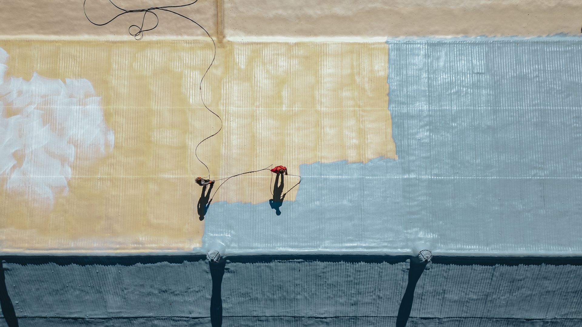 Overhead view: Two people painting a large surface in yellow and blue.