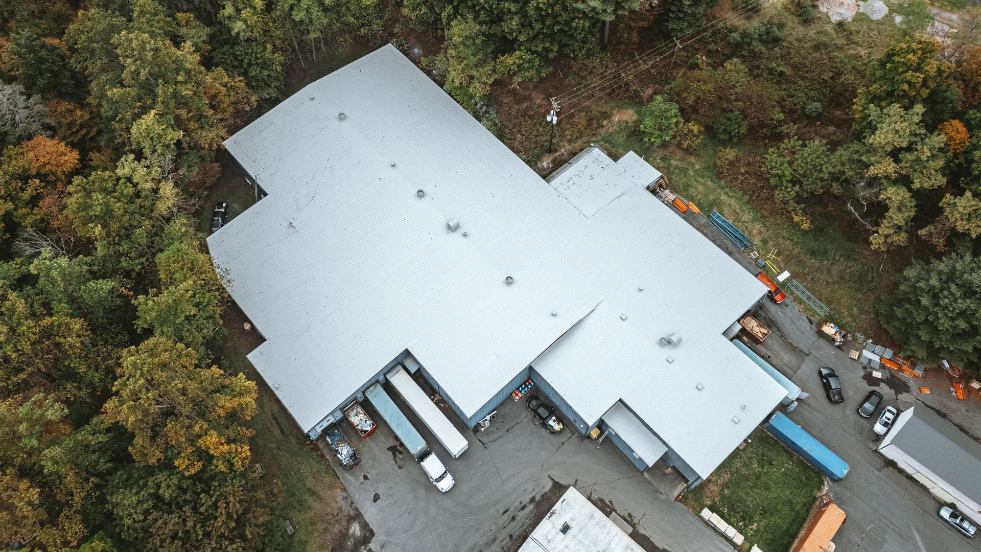 Aerial view of a warehouse with loading docks and trucks, surrounded by trees.