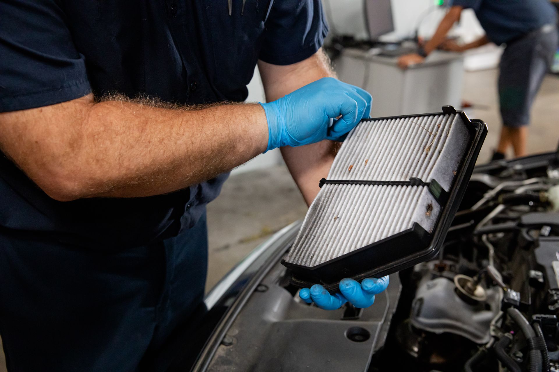 A man wearing blue gloves is holding a air filter in front of a car.