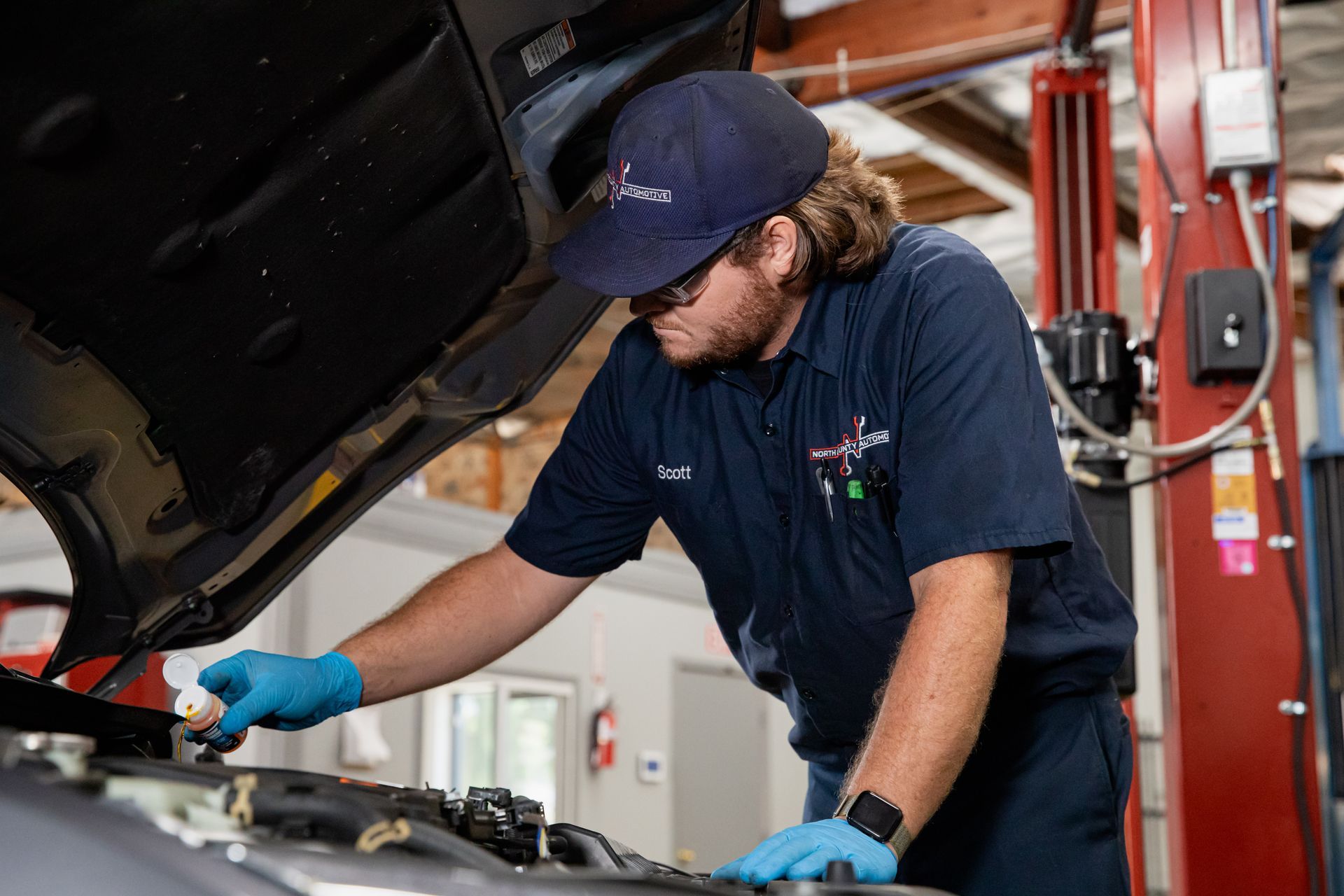 Mechanic in blue uniform and gloves inspecting a car engine in an auto repair shop