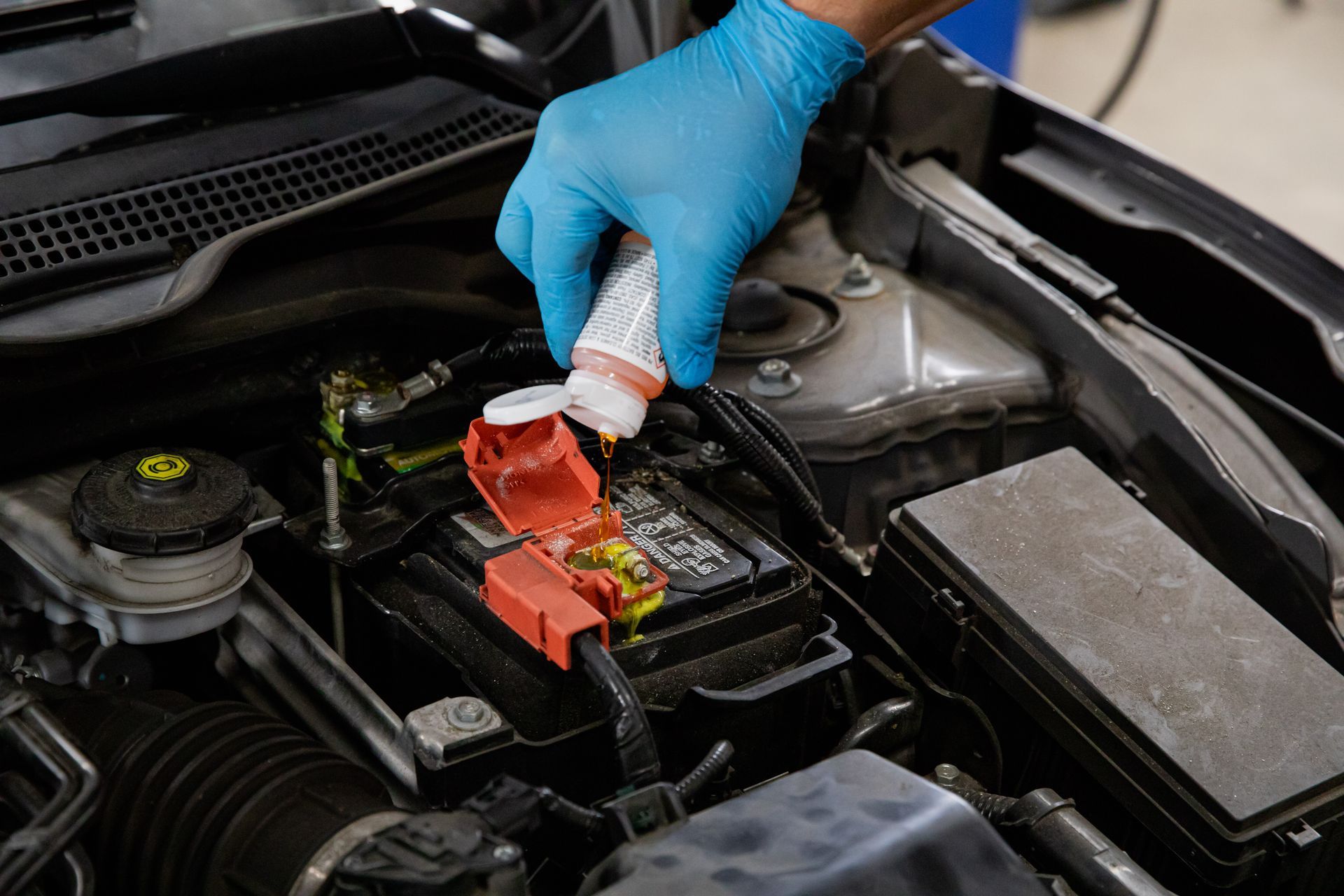 A person wearing blue gloves is working on a car battery.