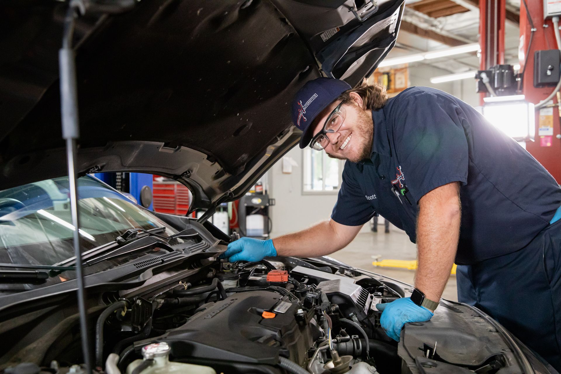 A man is working under the hood of a car in a garage.