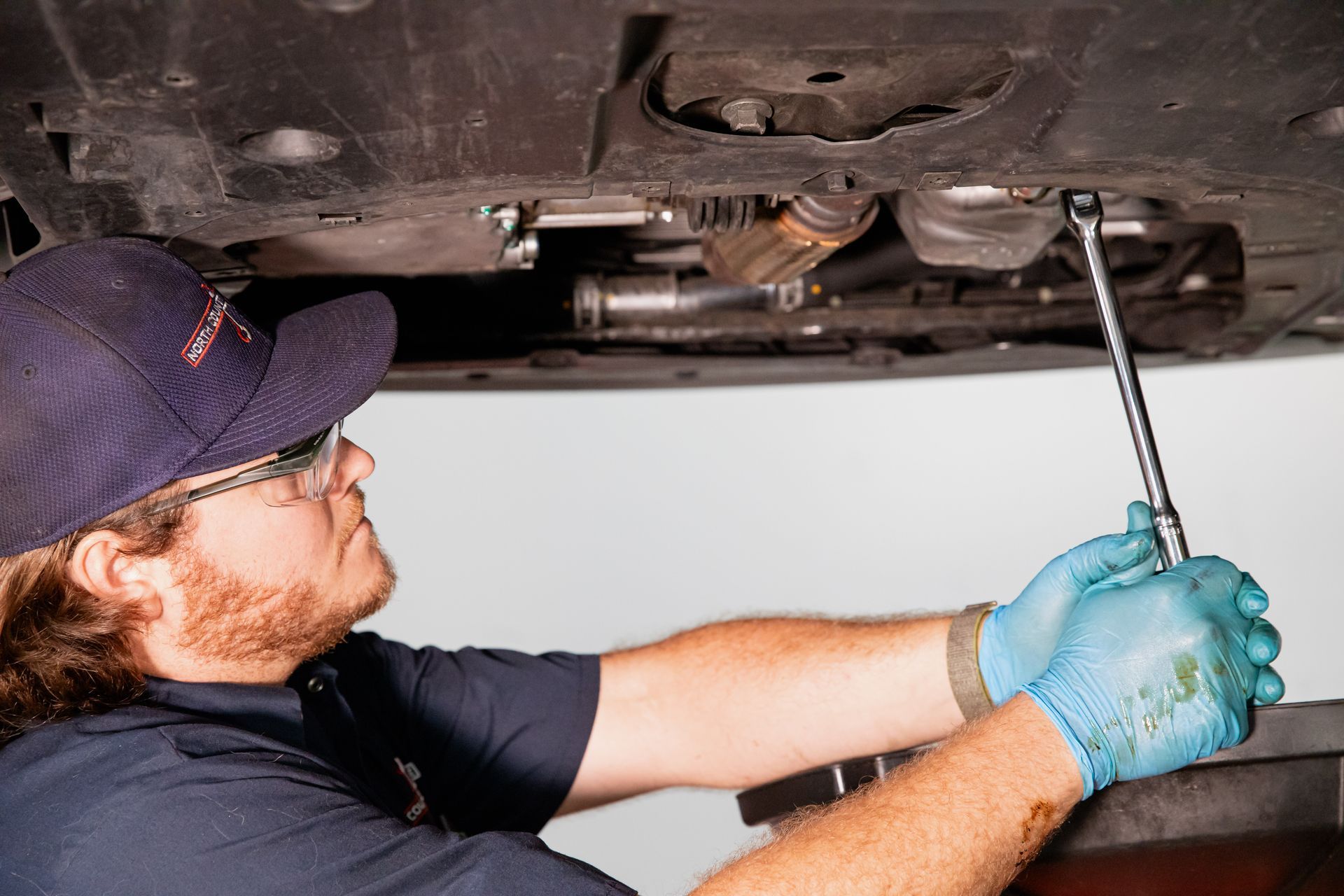 Mechanic in blue gloves using a wrench to work under a car on a lift