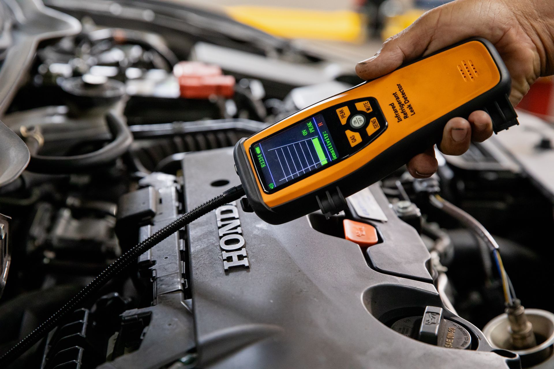 A person is holding a device over a car engine.
