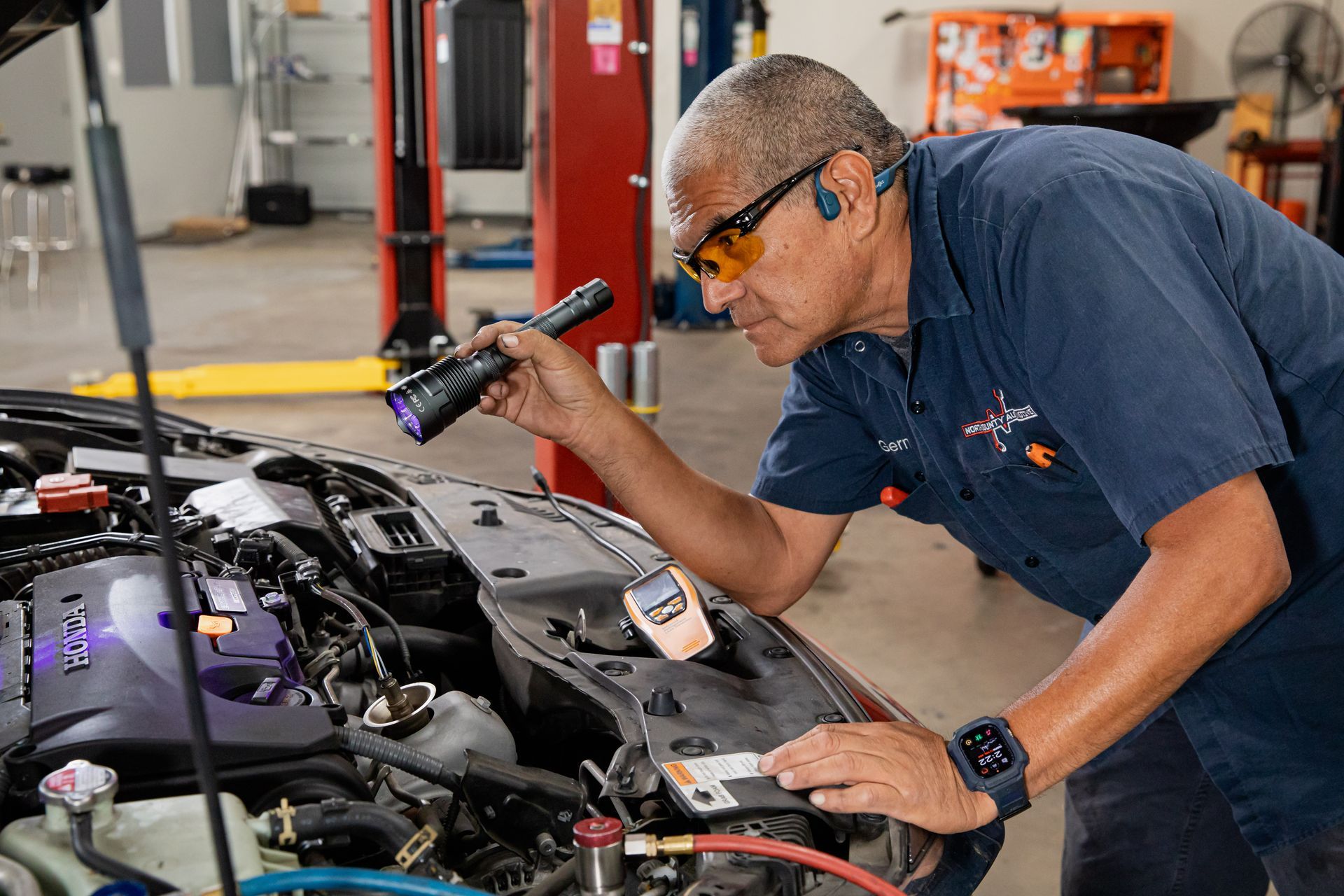 A man is looking under the hood of a car with a flashlight.