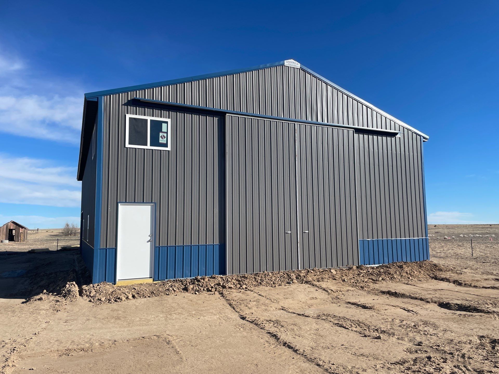 Tan and gray barn with a porch under a blue sky.