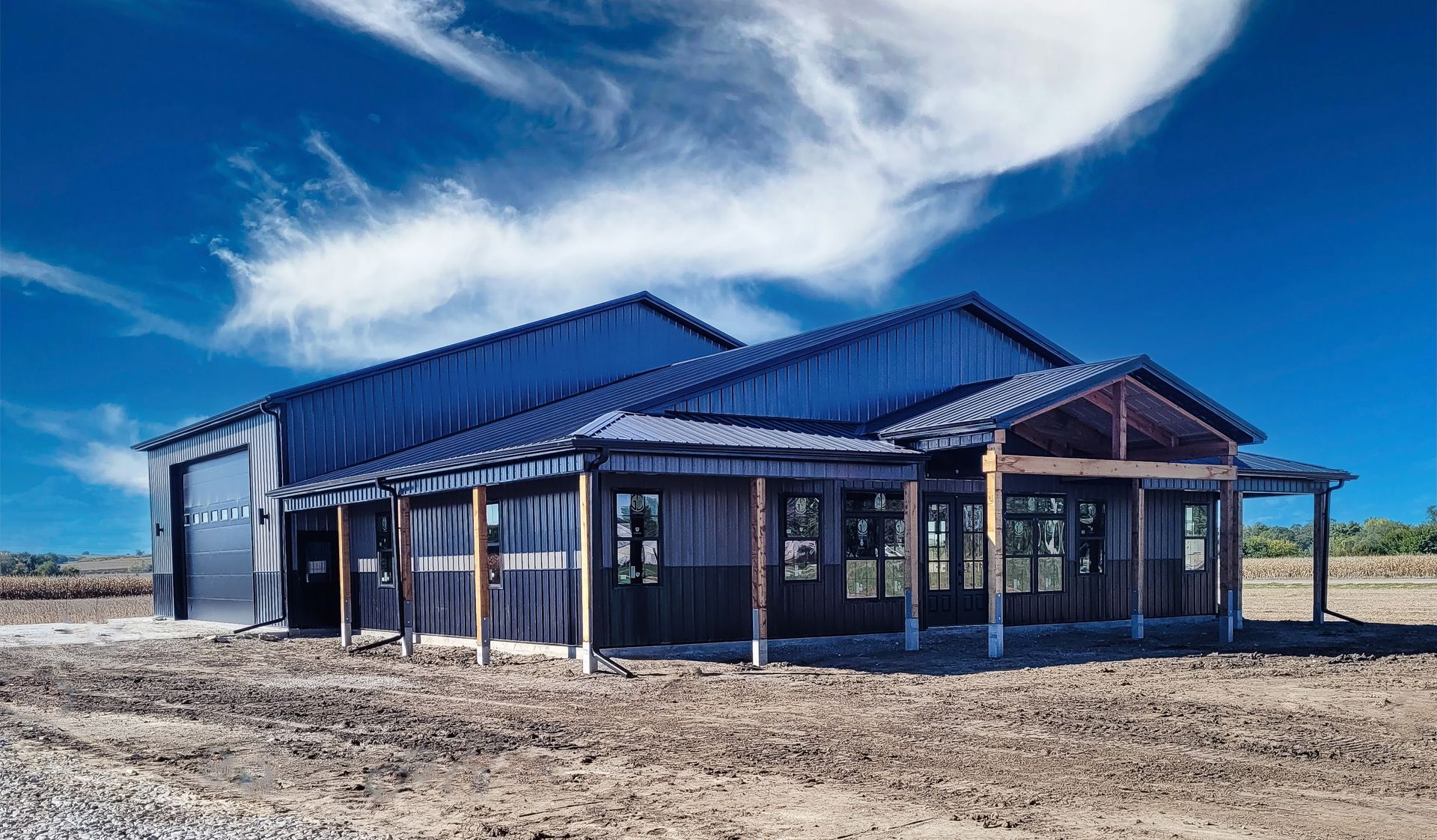 Barn-style building with a dark metal roof, open porch, and garage door under a bright blue sky.