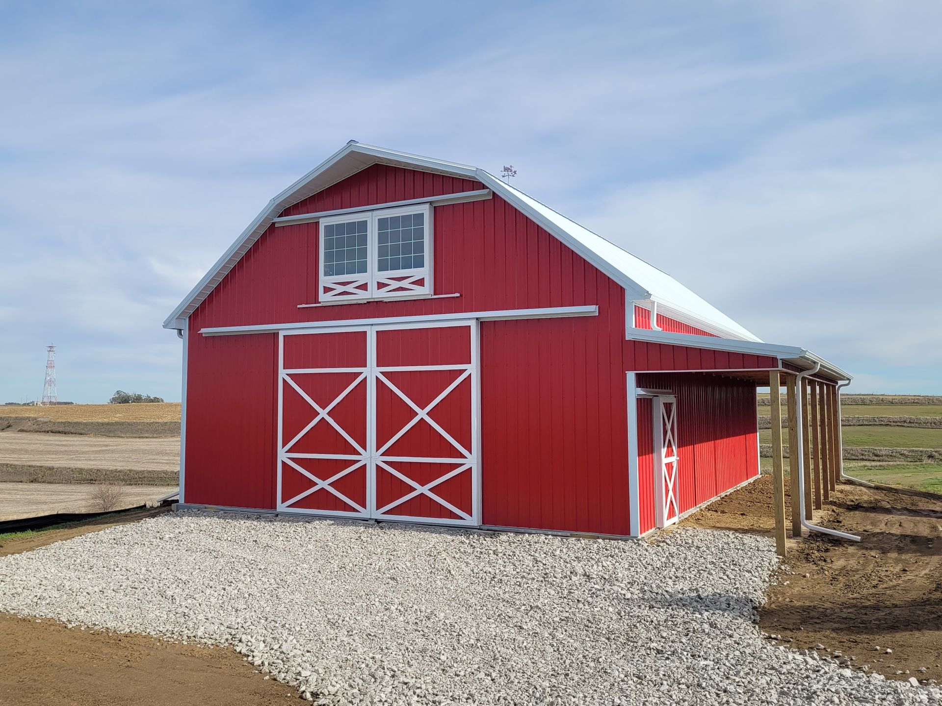 Red barn with white trim, a sliding door, and a covered side entrance on a gravel path, under a blue sky.