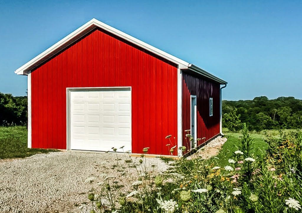 Red barn with white trim and garage door, gravel driveway, and sunny, green field.