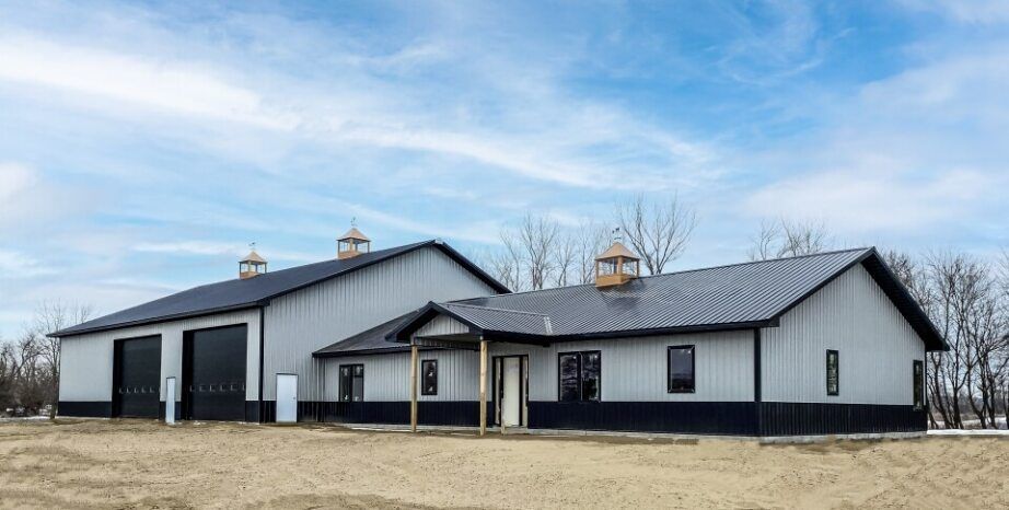 Gray and black barn-style building with three cupolas, under a partly cloudy sky.