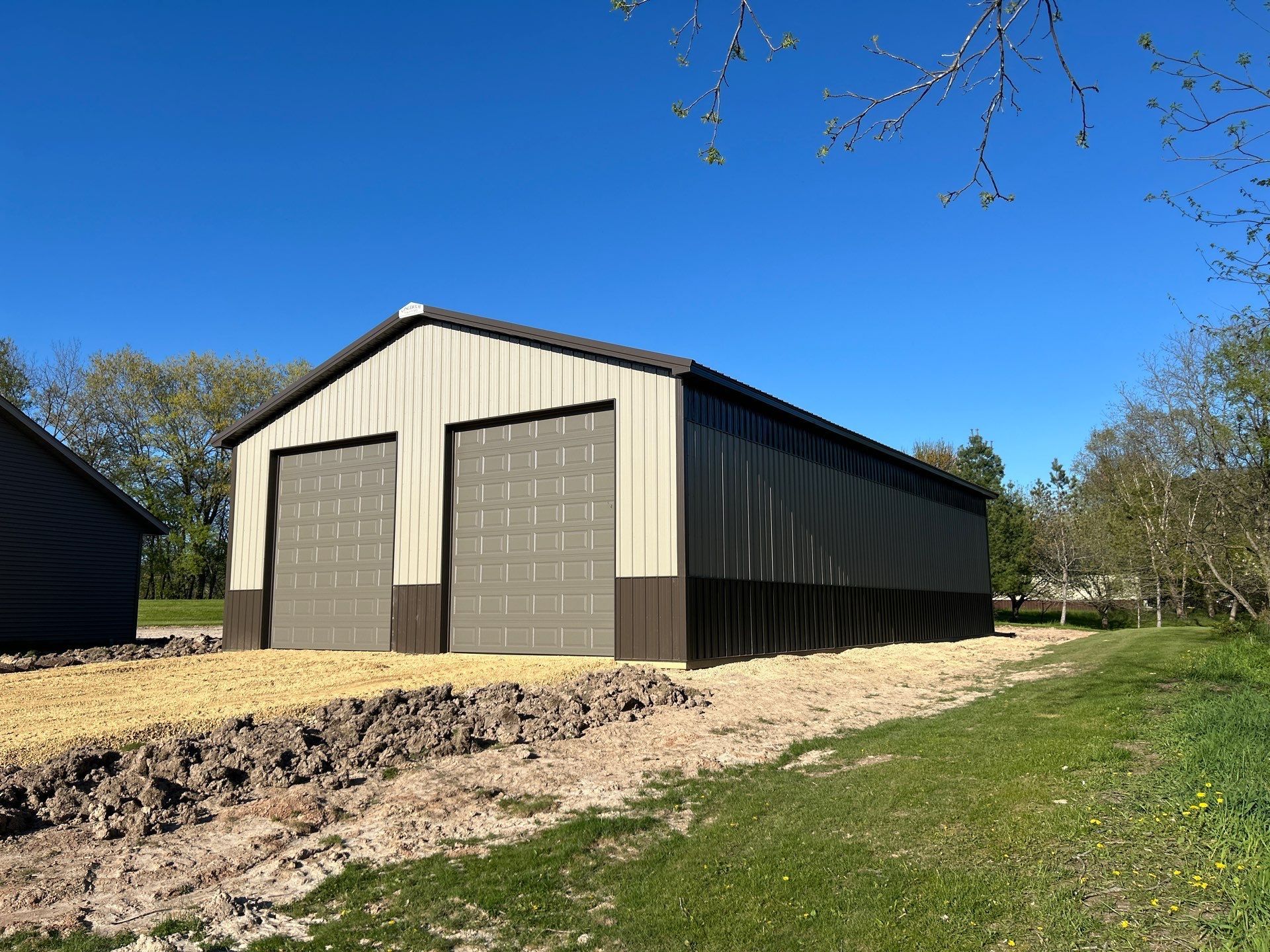 Red barn with metal siding under a blue sky. A tree is to the right.