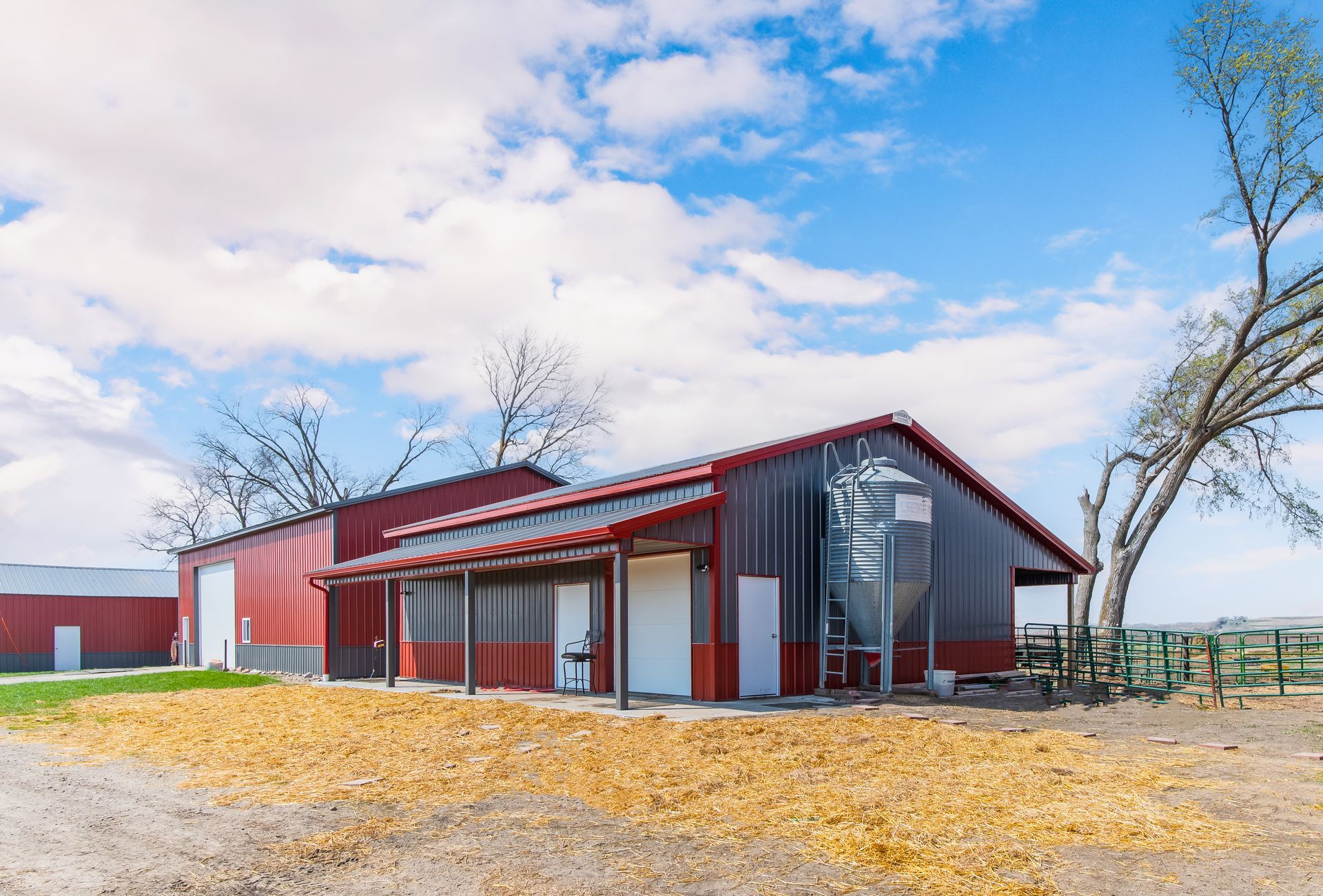 Red barn with white doors and awning, against a blue sky with clouds, rural setting.