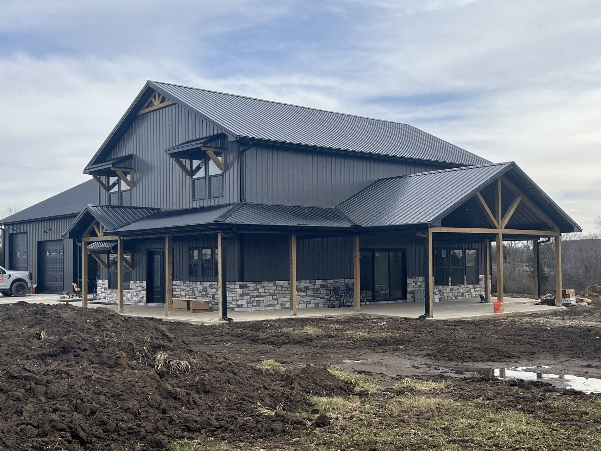 Dark gray barn-style house under construction, with a metal roof and stone accents.