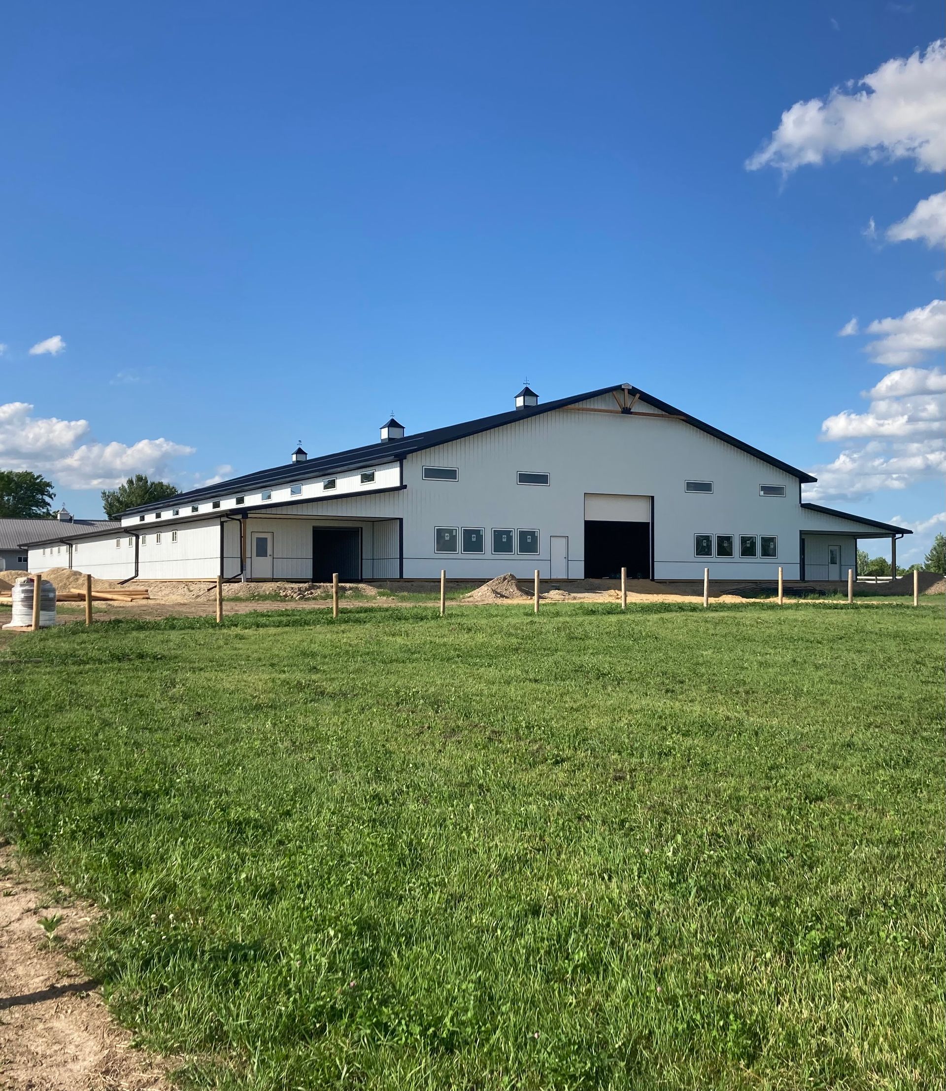 White barn with dark roof, surrounded by green grass under a blue sky with clouds.